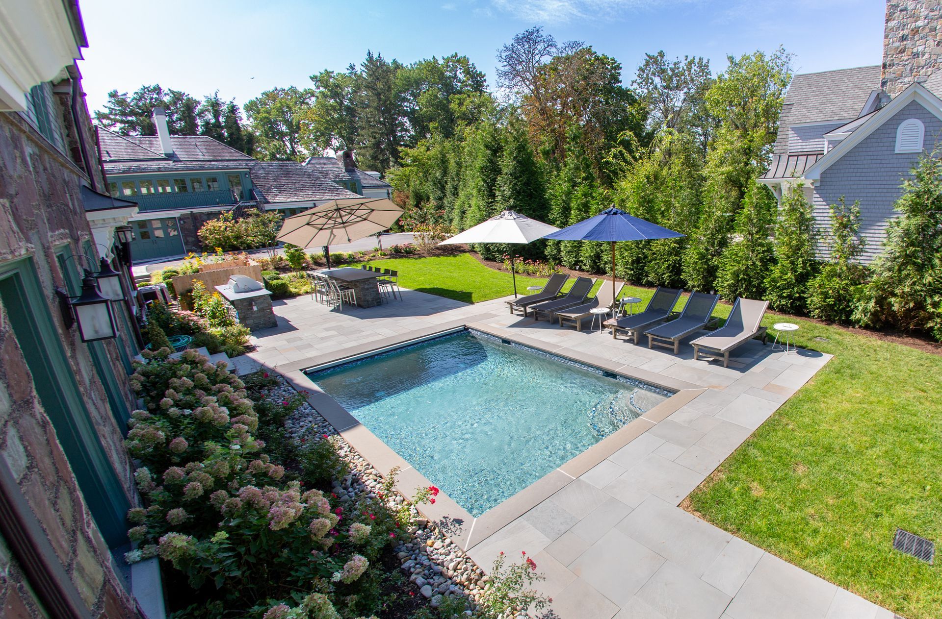 Backyard with pool, patio, lounge chairs, umbrellas, and manicured landscaping.