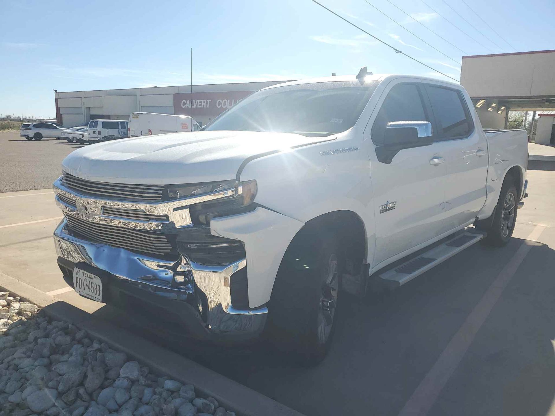 White pickup truck parked in a sunny lot with front-end damage and a crumpled bumper