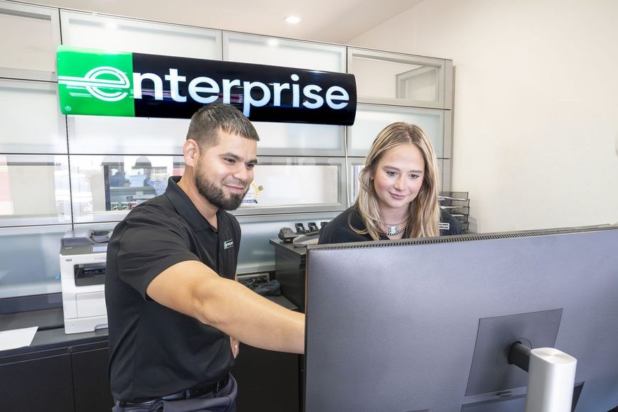 Two employees at an Enterprise counter reviewing a computer screen in a rental office