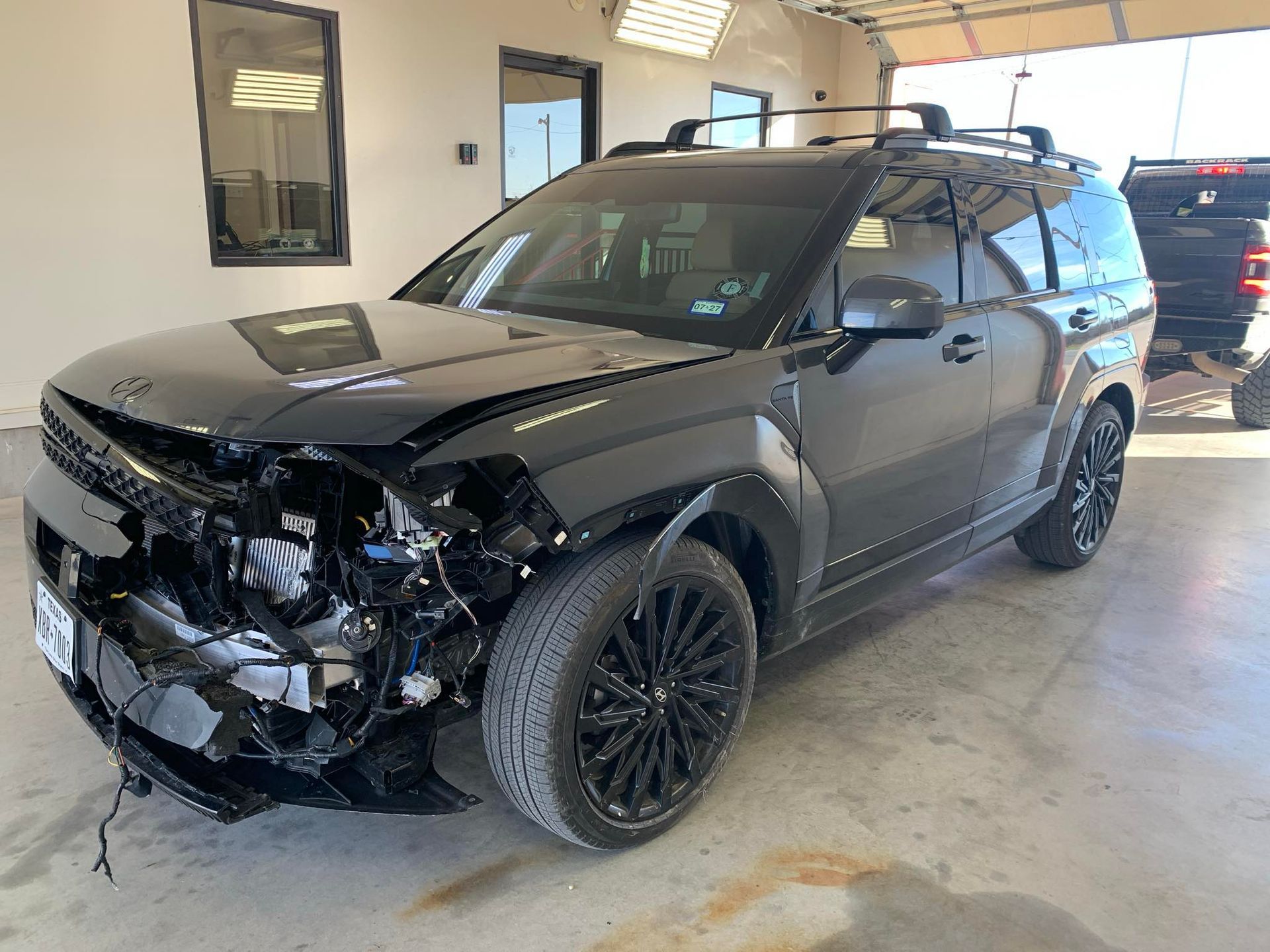 Black SUV with severe front-end damage parked in an auto repair shop.