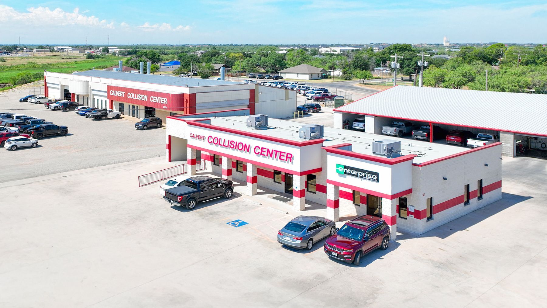 Aerial view of a red-and-white auto dealership with parked cars and a service lot