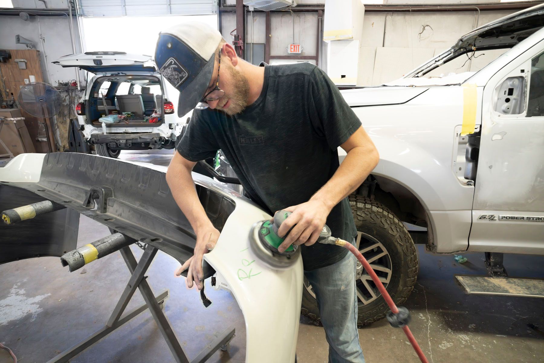 Worker sanding a white car body panel in an auto repair shop