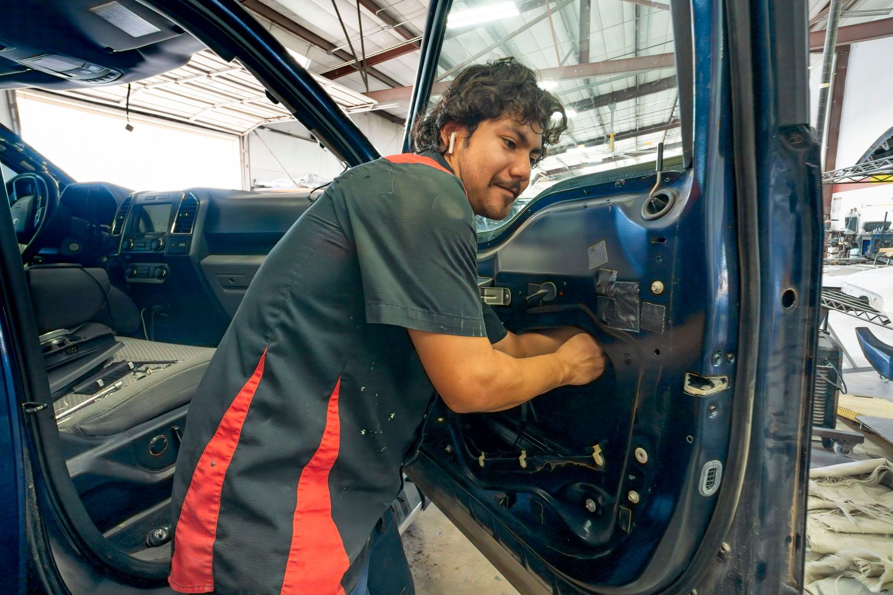 Mechanic working inside a blue car’s interior in a garage, smiling at the camera