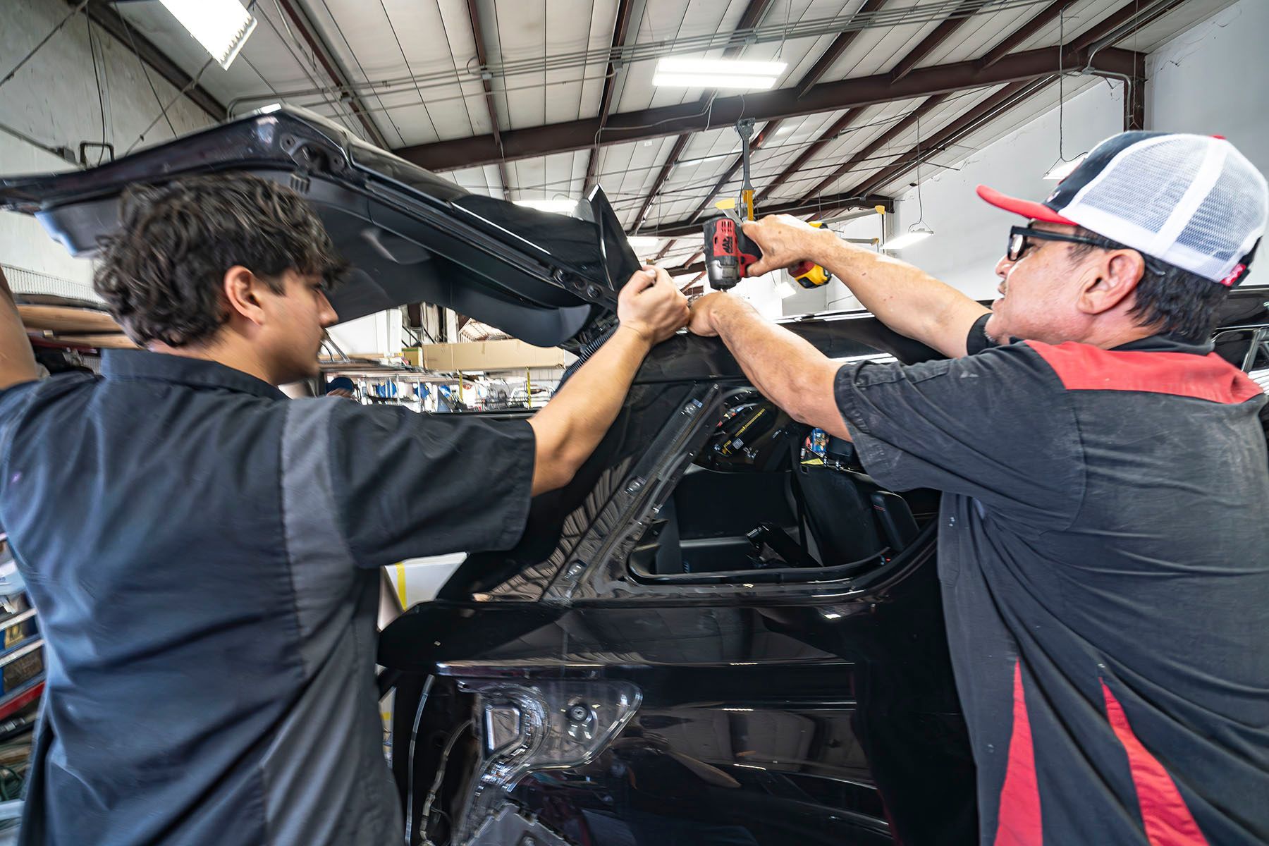 Two workers using tools to repair a black car frame in a garage