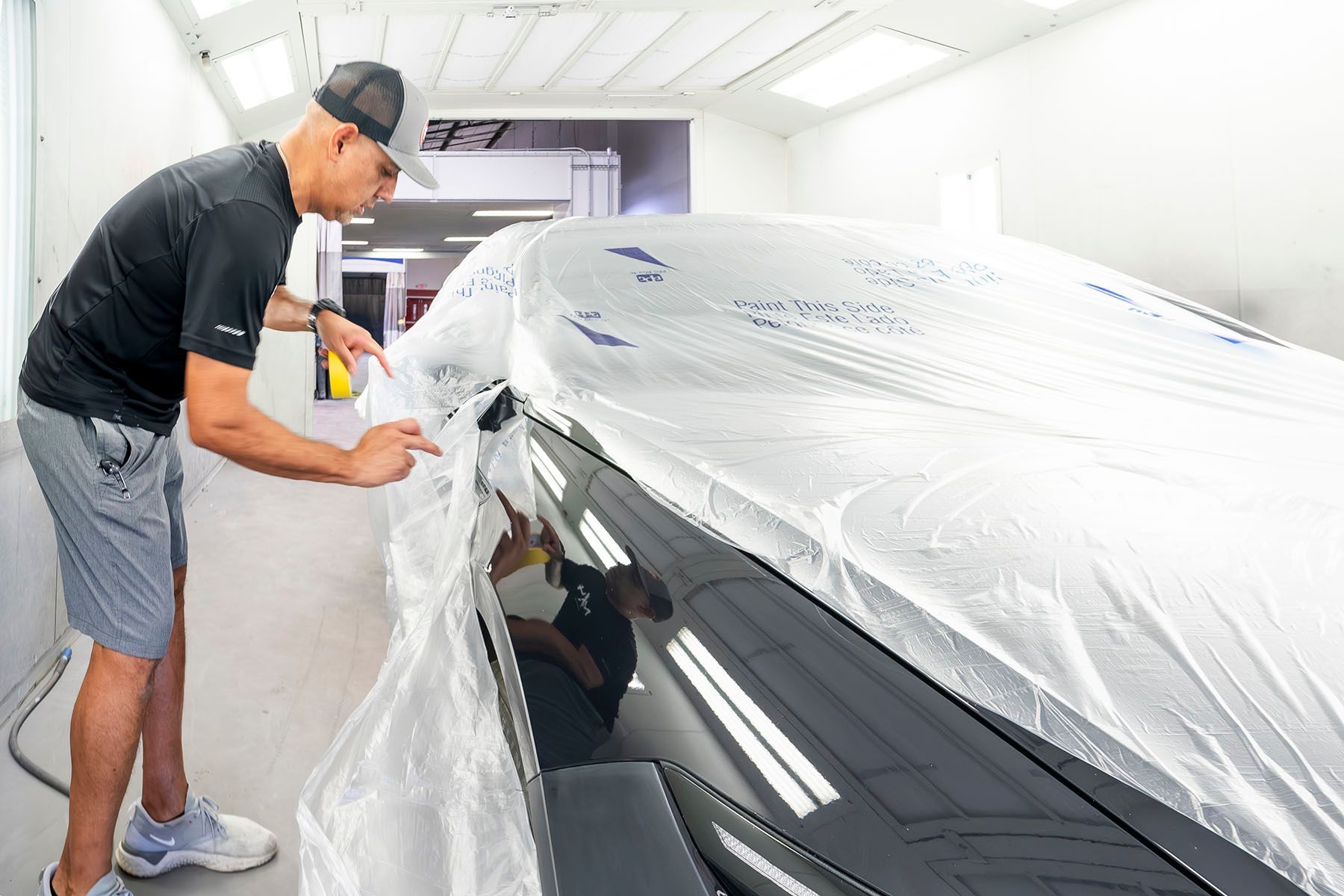 Man wrapping a black car in clear protective film in a bright auto shop