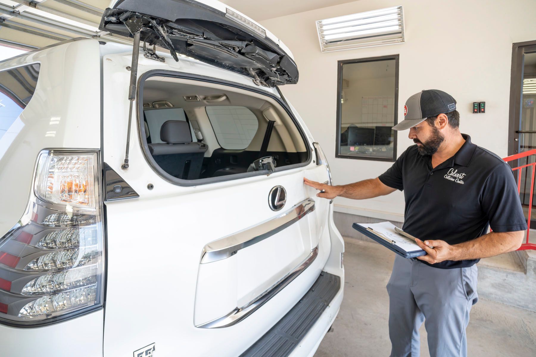 Technician inspecting the rear of a white SUV in a bright service bay
