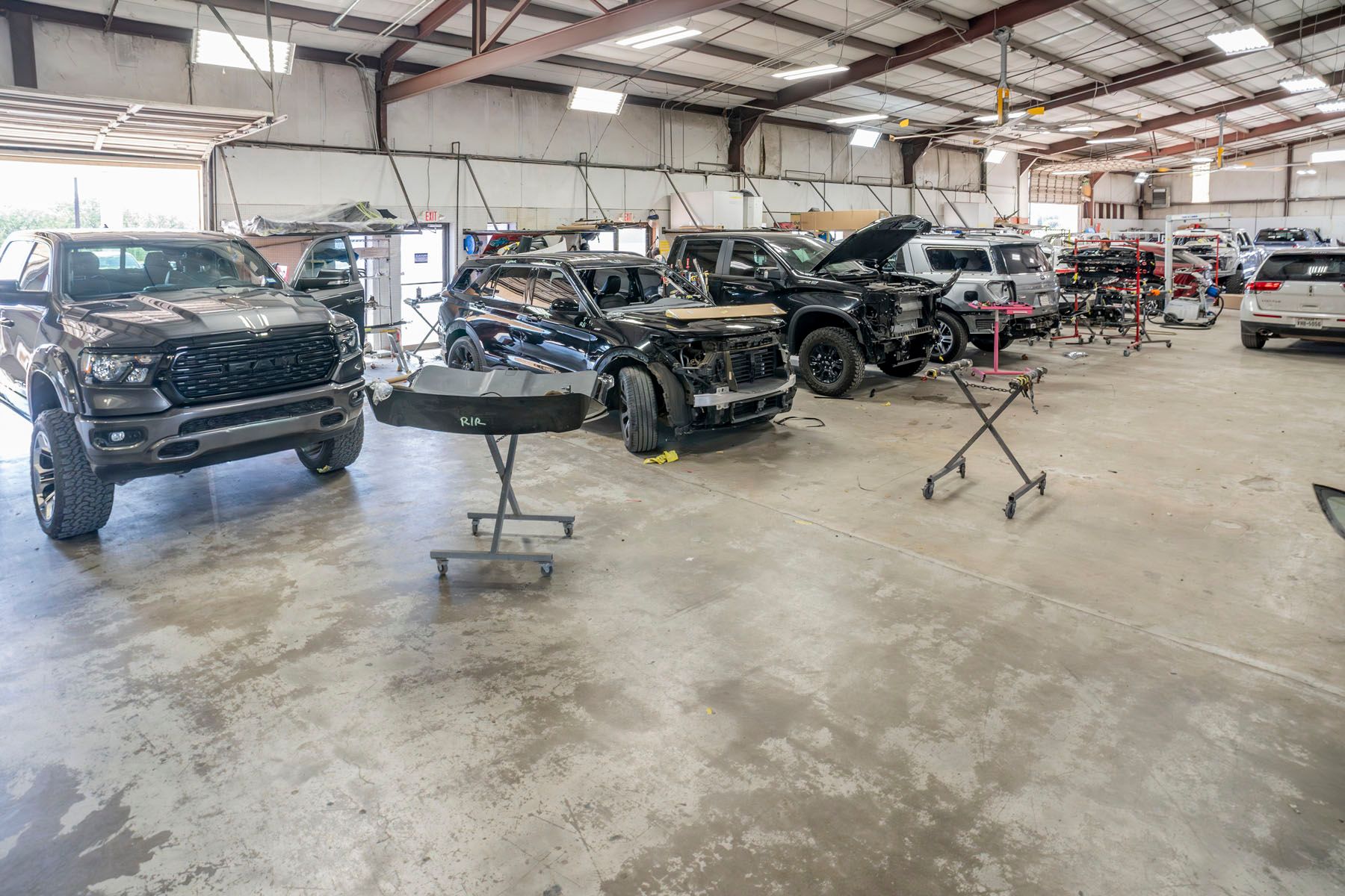 Vehicle repair shop with several damaged black SUVs and cars inside a warehouse-like garage
