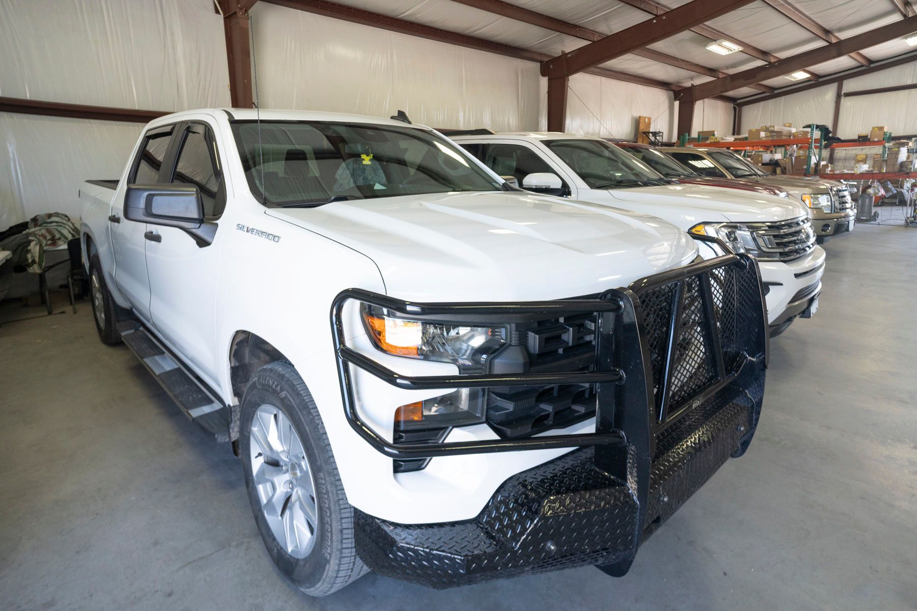 White pickup trucks parked indoors in a warehouse, front truck with black grille guard.