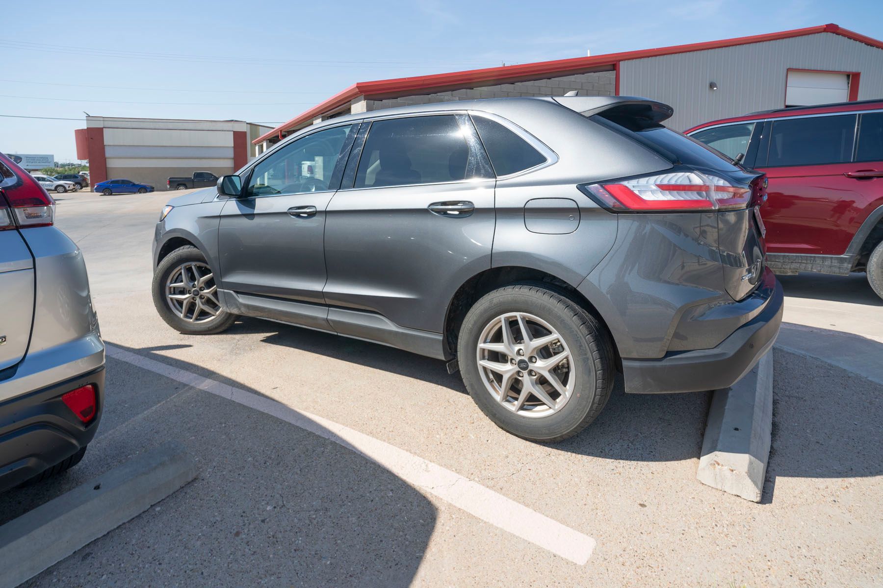 Gray SUV parked in a sunny lot beside red and blue cars