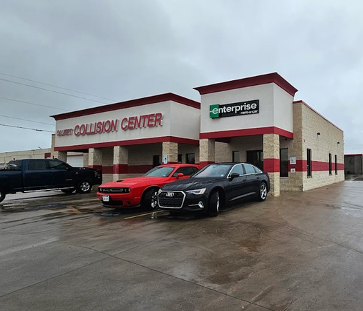 Car rental collision center building with three parked vehicles on a wet lot