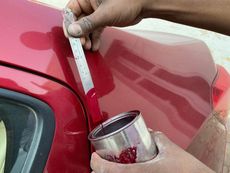 Hands painting red car panel with a brush and metal paint cup