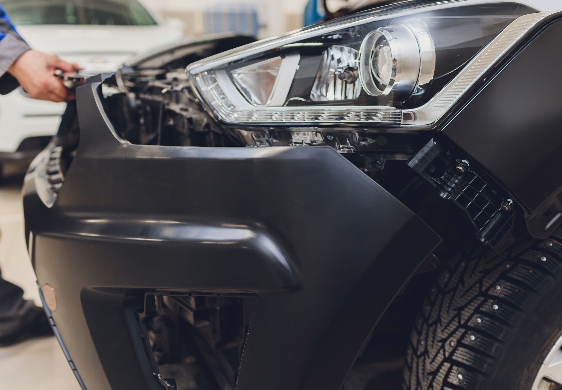 Close-up of a black car front bumper and headlight during repair in an auto shop