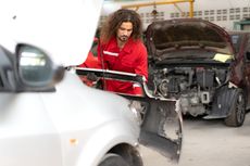Mechanic in red jacket inspecting a damaged car in a repair shop