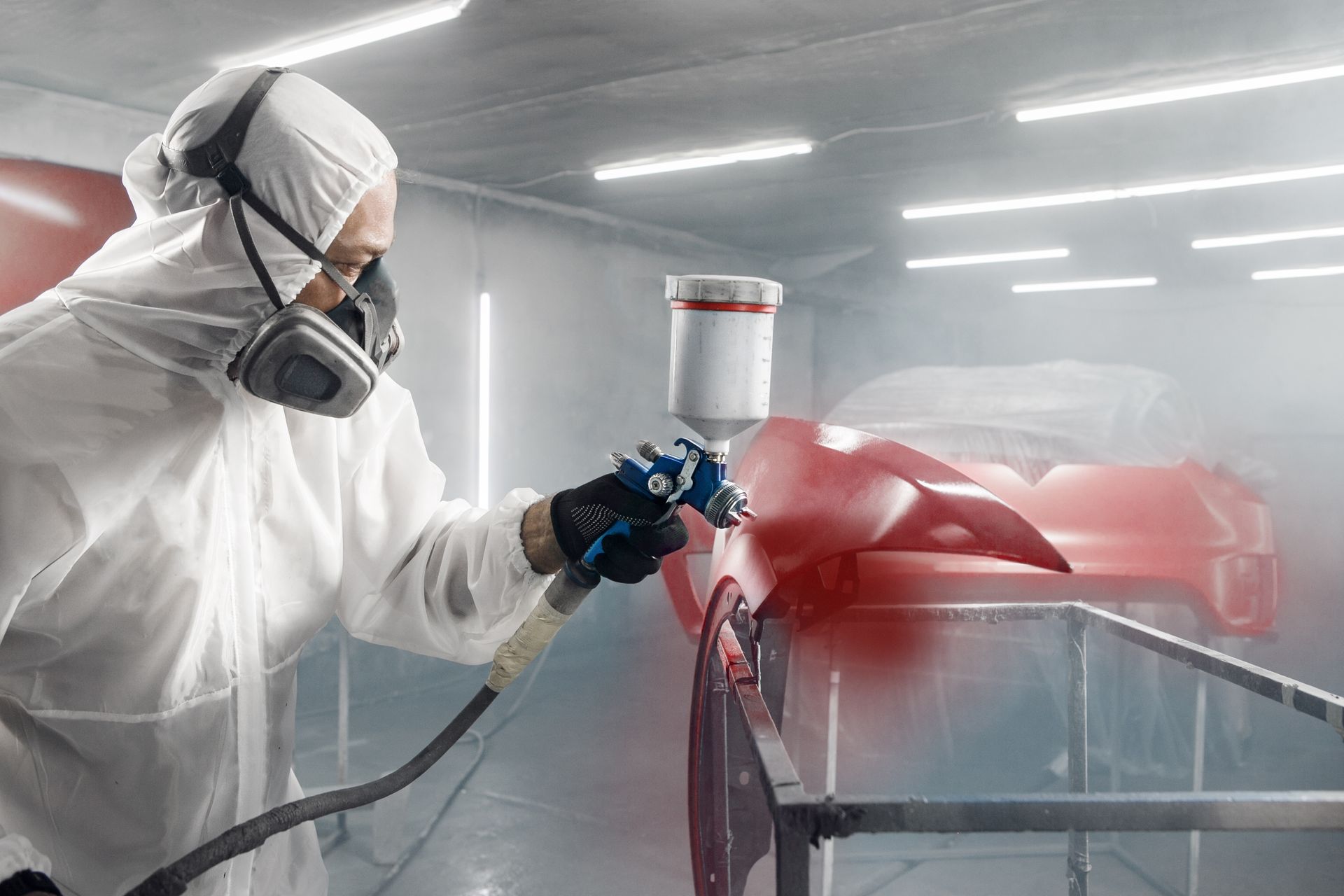 Worker in protective suit spray-painting a red car in a paint booth