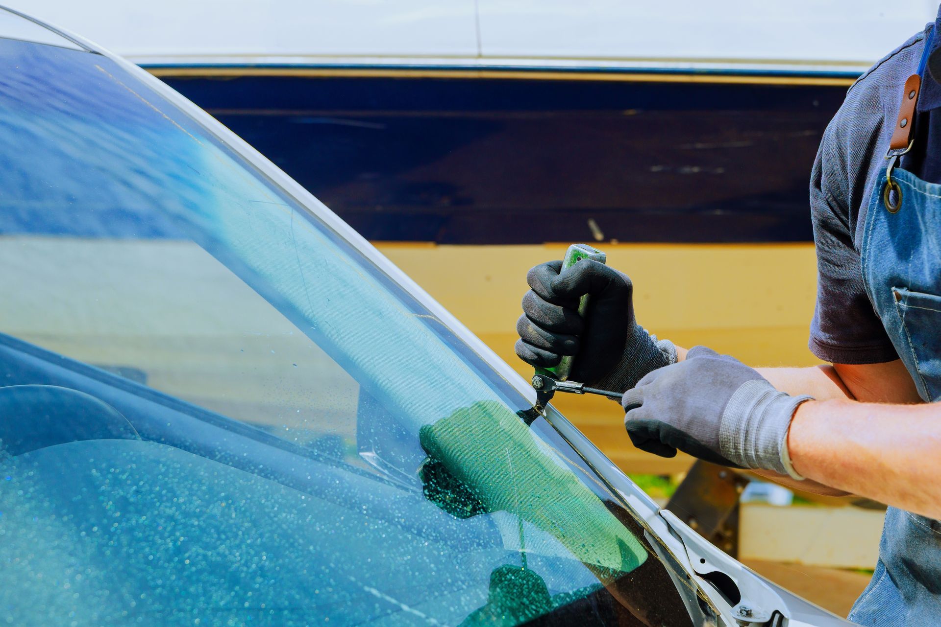 Worker repairing a car windshield with a power tool outdoors