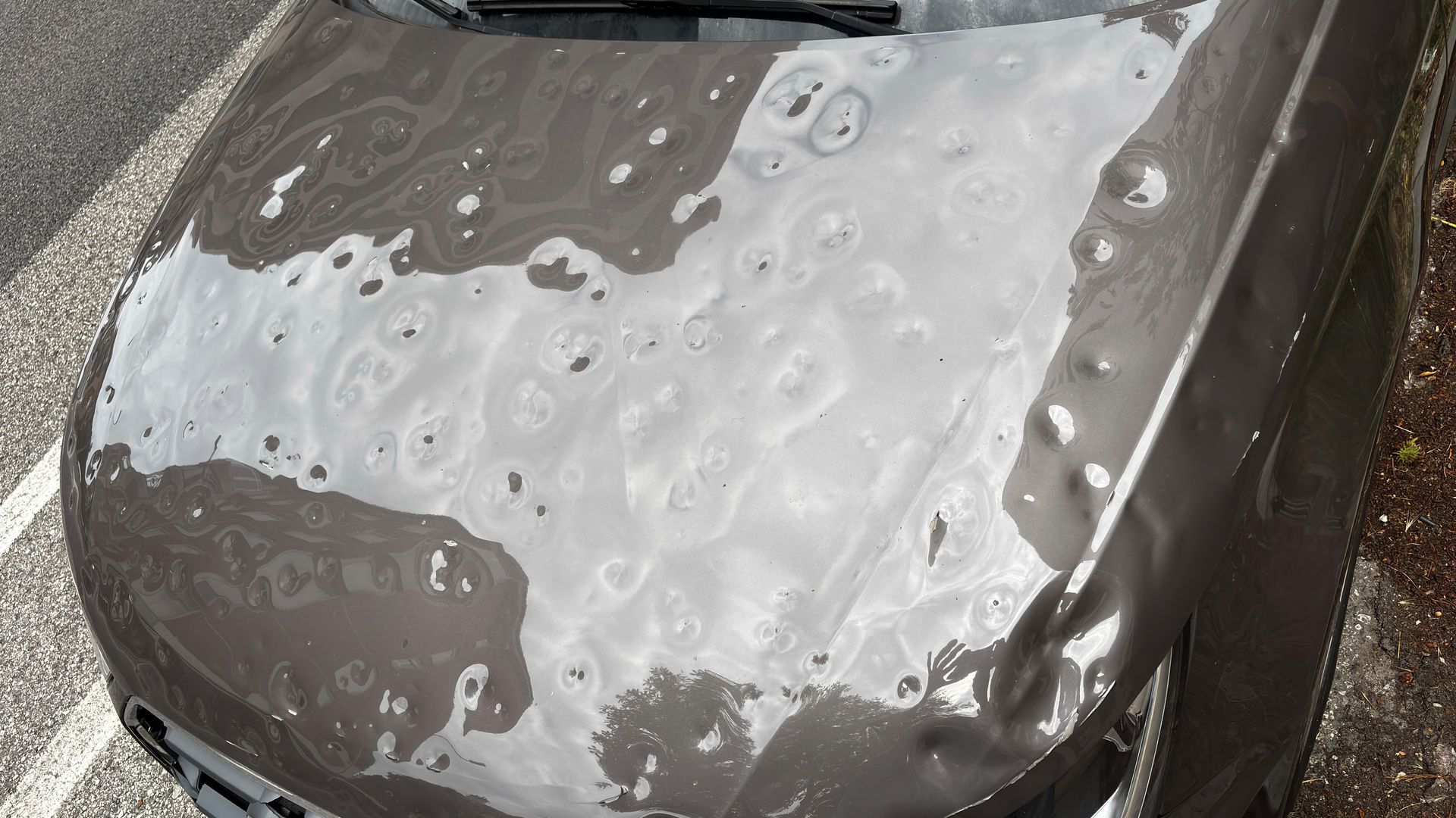 Rain-covered black car hood with large water droplets in a parking lot