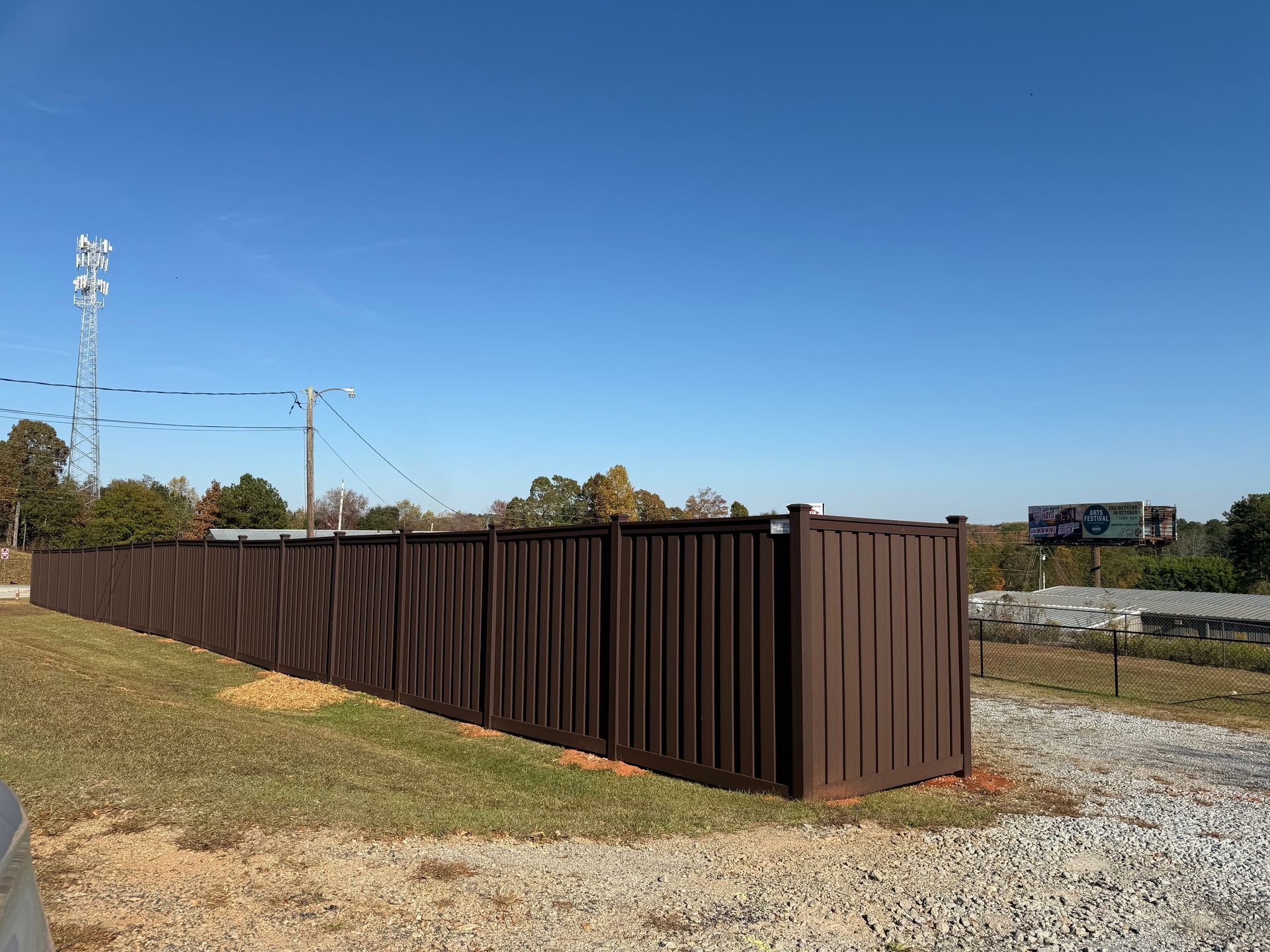 Long brown metal dumpster enclosure beside a gravel lot under a clear blue sky