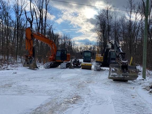 Engins de chantier sur un sol enneigé dans une zone boisée sous un ciel nuageux.