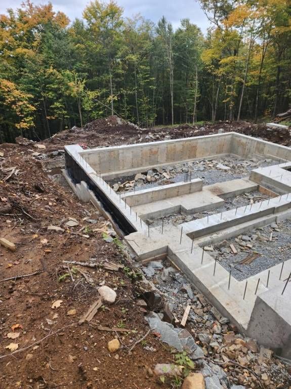 Fondations d'un bâtiment en construction, posées sur la terre, avec des arbres en arrière-plan.
