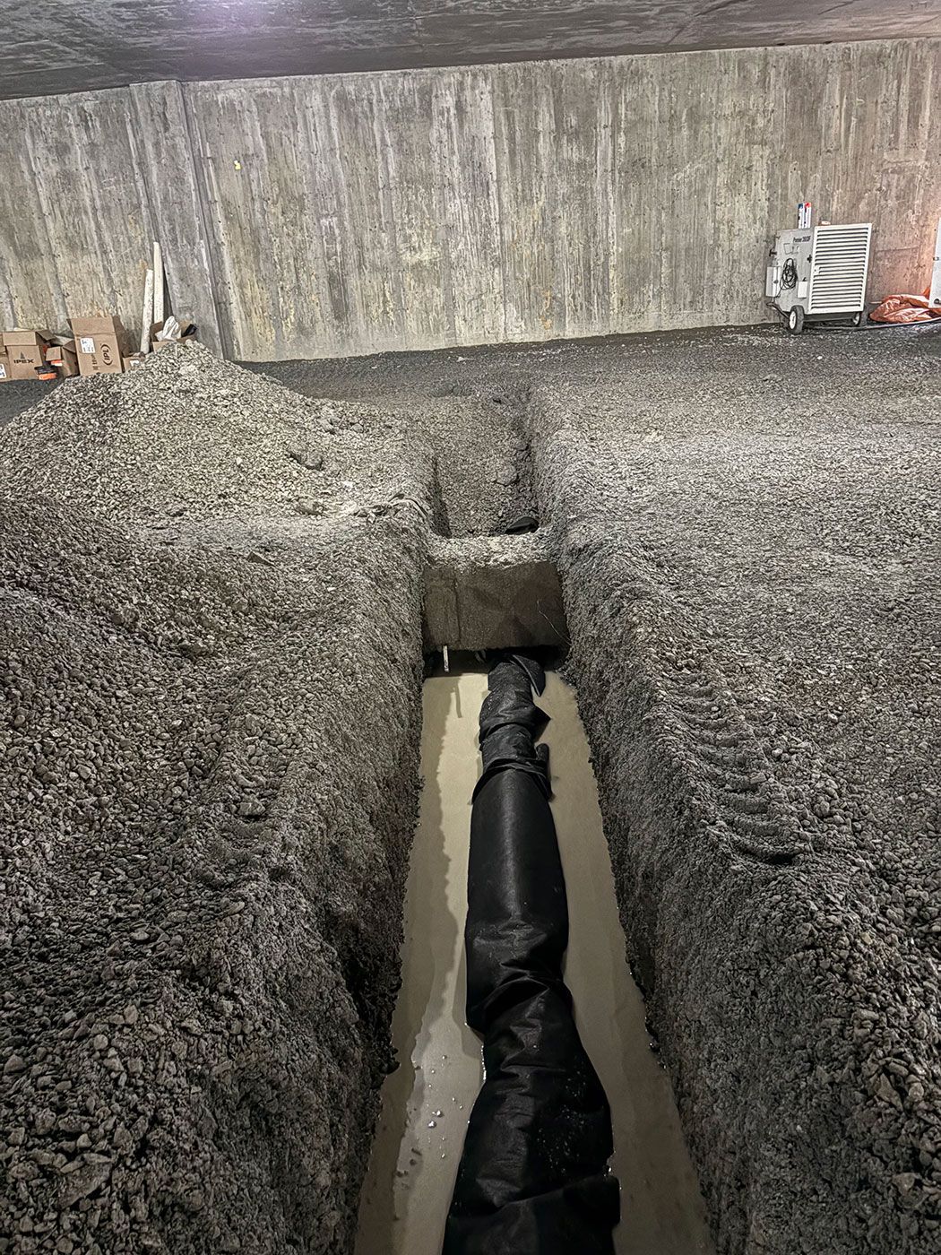 Tranchée avec tuyau noir et gravier, probablement un chantier de construction à l'intérieur d'un tunnel, parois en béton.