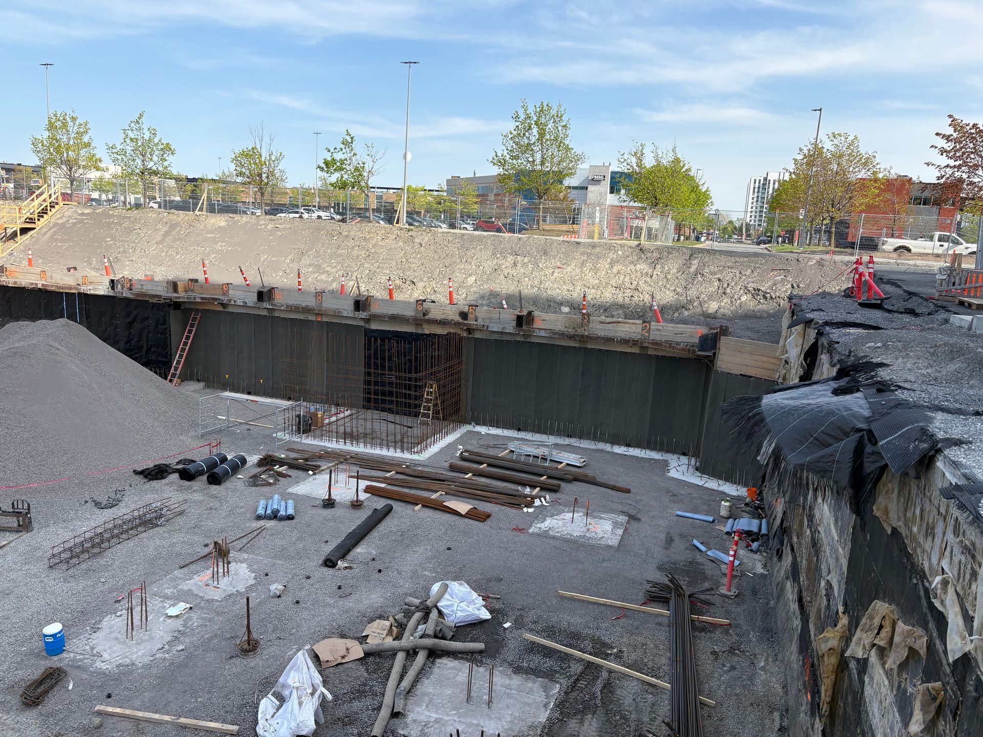 Chantier de construction avec d'importantes excavations, des murs de soutènement, du gravier et des matériaux de construction.
