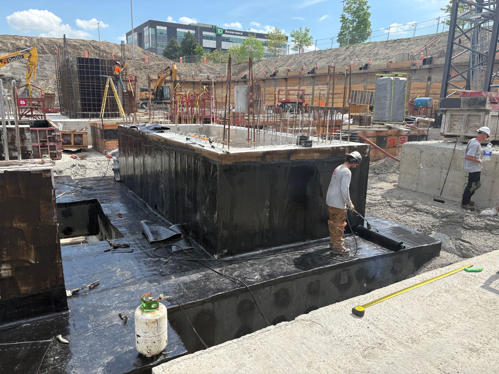 Chantier de construction : des ouvriers appliquent du mastic sur une structure en béton ; divers matériaux de construction et un bâtiment en construction sont visibles.