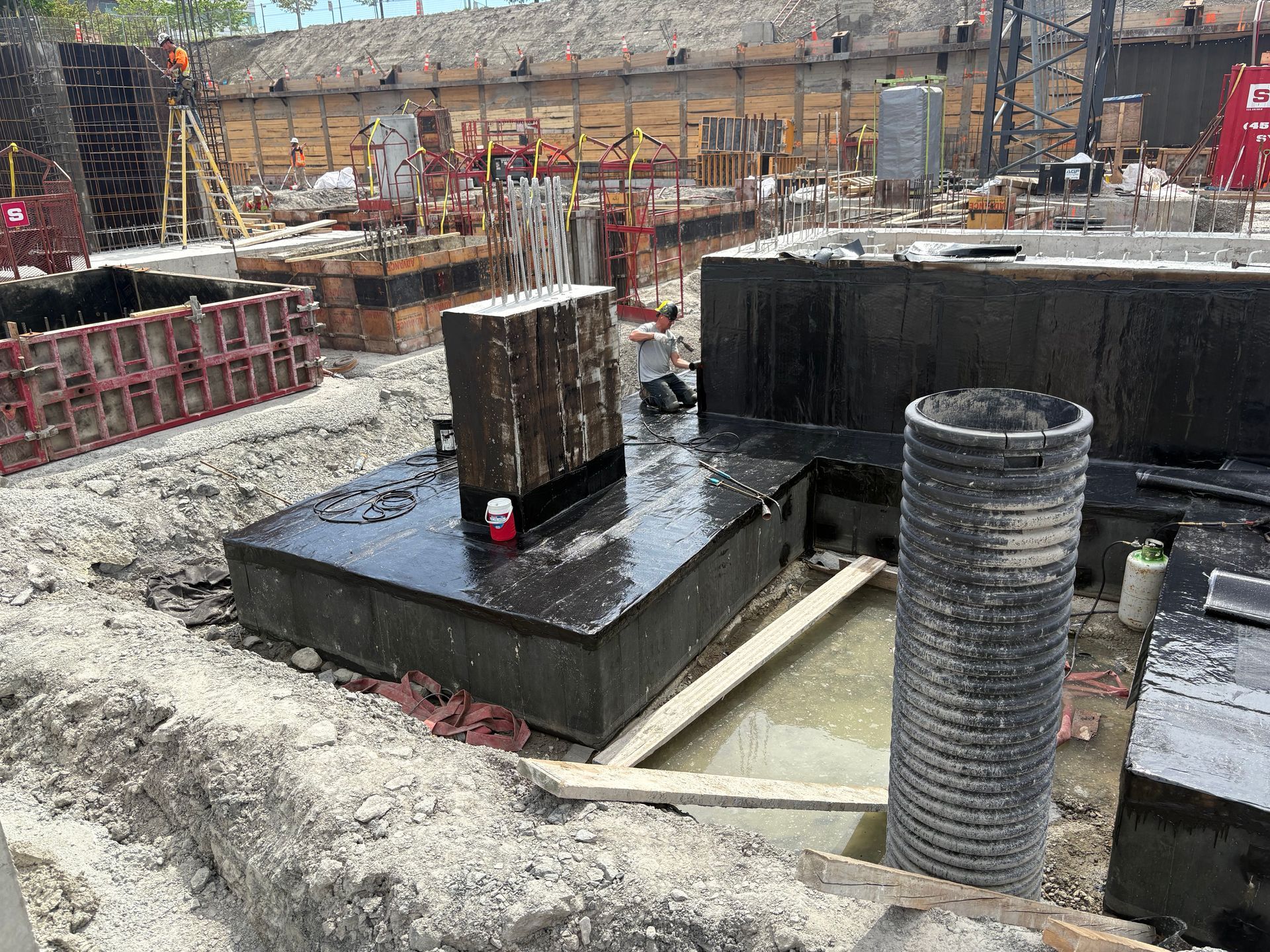 Chantier de construction avec des structures en béton, des coffrages en bois et un tuyau cylindrique.