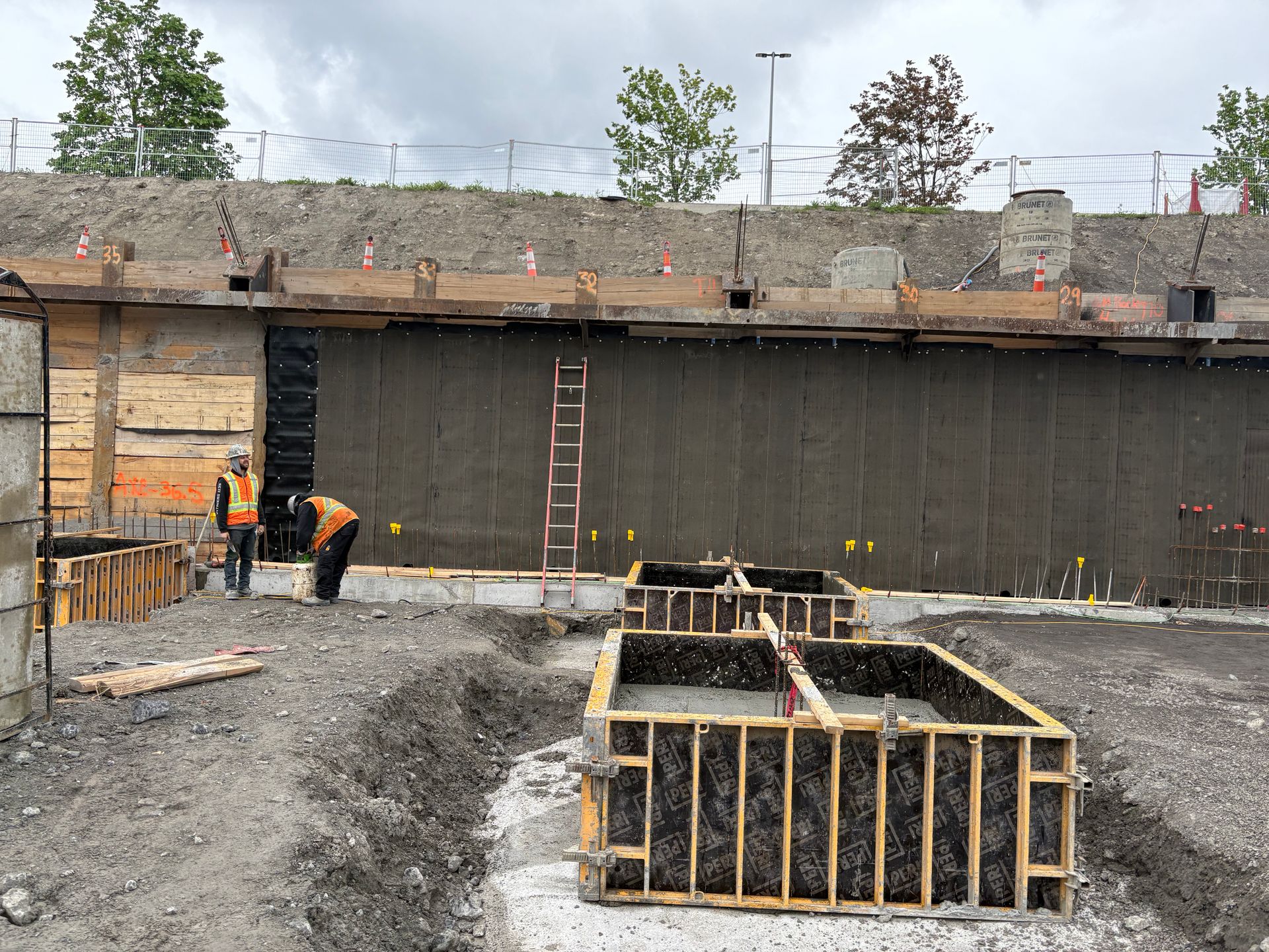 Des ouvriers du bâtiment construisent des structures en béton à l'extérieur. Mur gris, coffrages en bois, ciel nuageux.