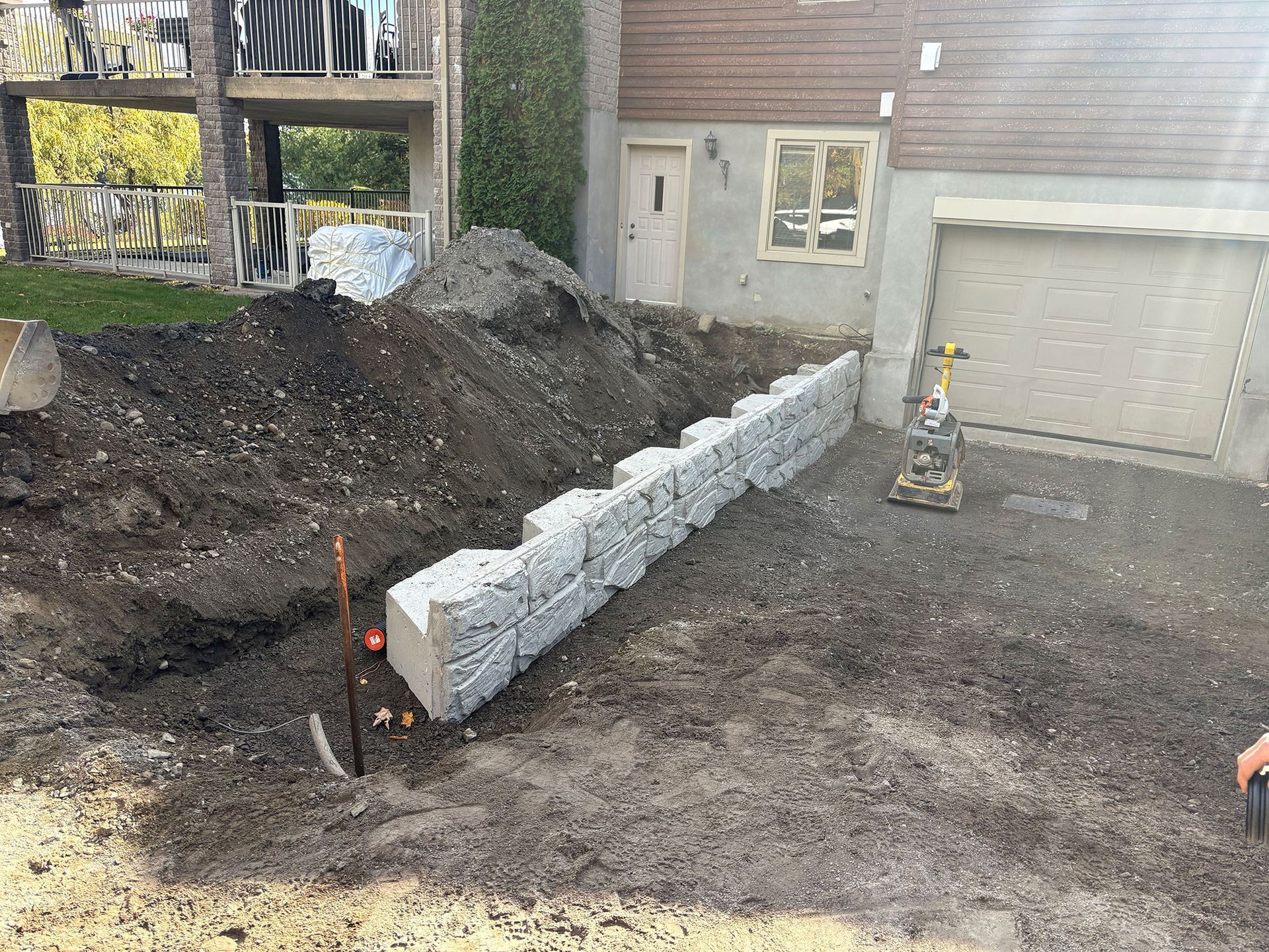 Chantier de construction avec un mur de gabions en construction à côté d'une maison avec garage.