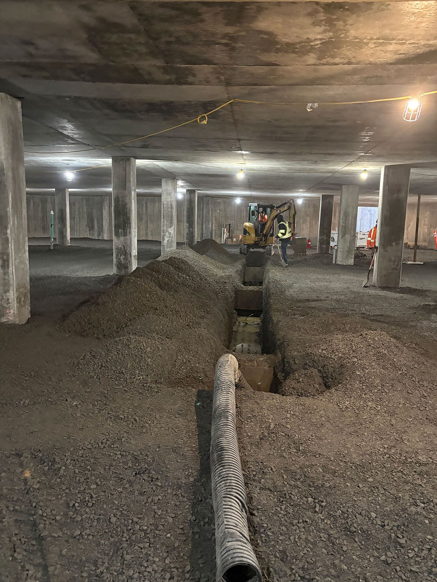 Chantier : sol en béton avec tranchées, piliers et pelle mécanique.
