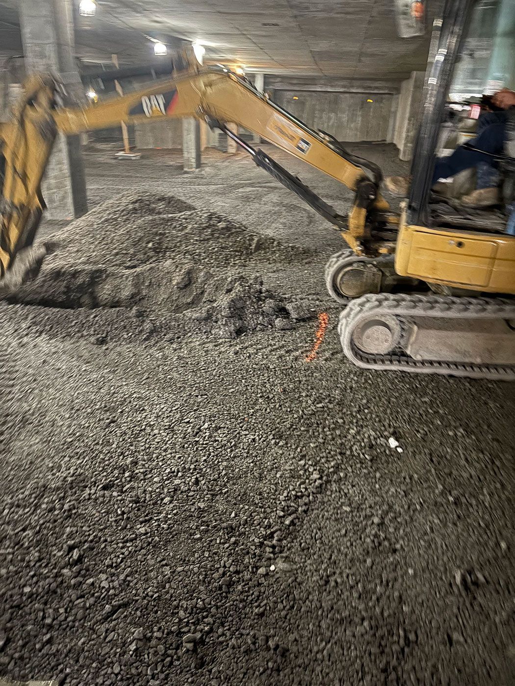 Une pelleteuse jaune creuse dans un chantier de construction intérieur poussiéreux.