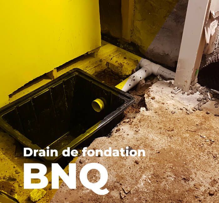 Fossé de drainage noir dans un coin de fondation peint en jaune. Un tuyau blanc y est raccordé. On aperçoit de la terre brune et du béton.