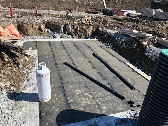 Chantier de construction avec fondations en béton, réservoir de propane et tuyaux noirs.