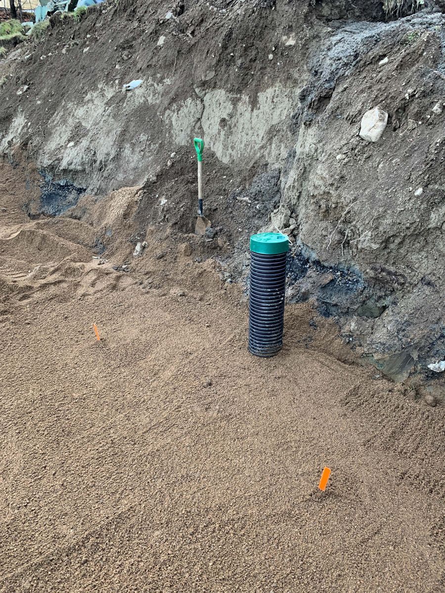 Chantier de construction avec un tuyau ondulé noir et un bouchon vert, de la terre et des débris.