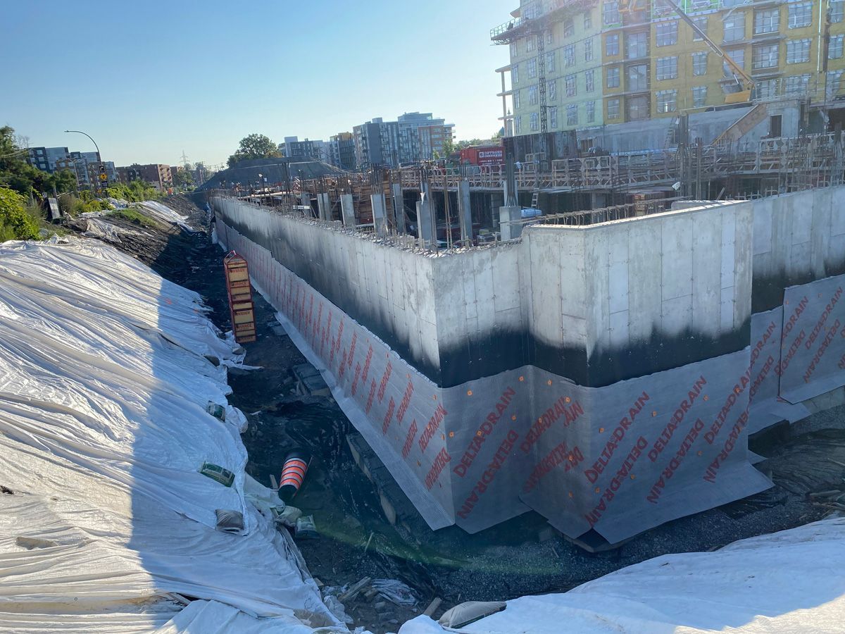 Chantier de construction avec un mur de soutènement en béton recouvert d'un matériau noir et orange.
