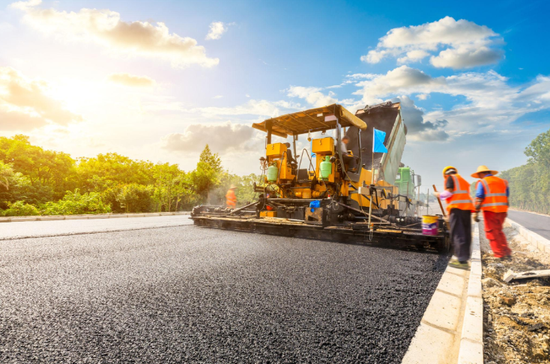 “Road crew working beside a paving machine laying fresh asphalt on a wide roadway during an asphalt service in Fulshear, TX”