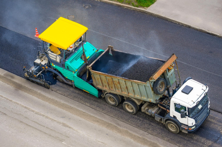 “Aerial view of a dump truck feeding asphalt into a paving machine on a roadway during an asphalt service in Fulshear, TX”