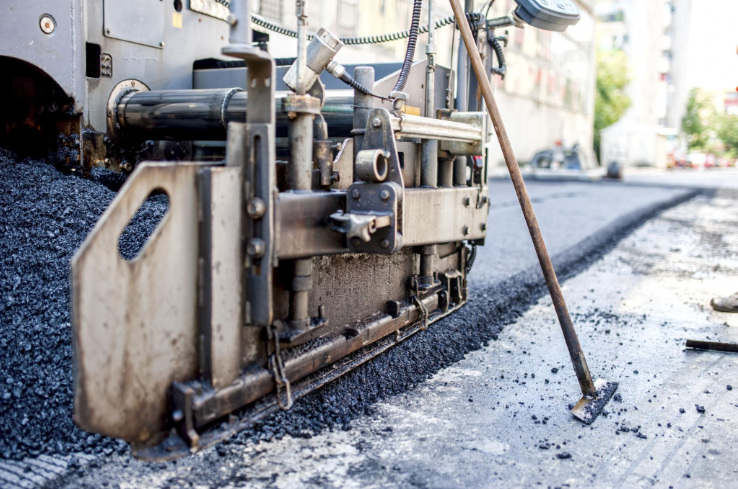 “Close-up of paving equipment spreading fresh black asphalt evenly across a road surface during an asphalt service in Fulshear, TX”