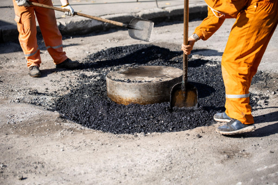 “Workers filling and leveling a damaged asphalt area with hot patch material during an asphalt service in Fulshear, TX”