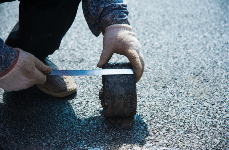 “Close-up of a worker using a hammer and tool to inspect asphalt surface condition during an asphalt service in Fulshear, TX”