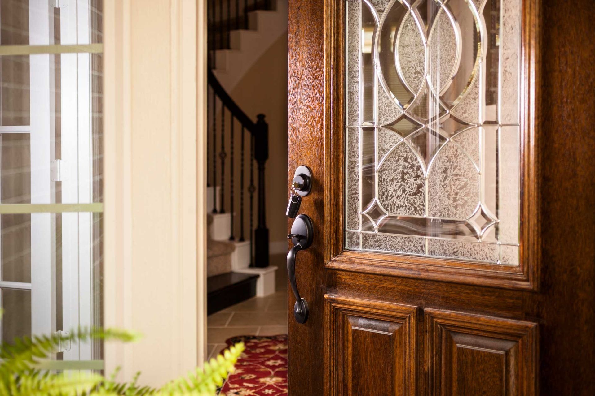A wooden door with a stained glass window is open to a hallway with stairs.