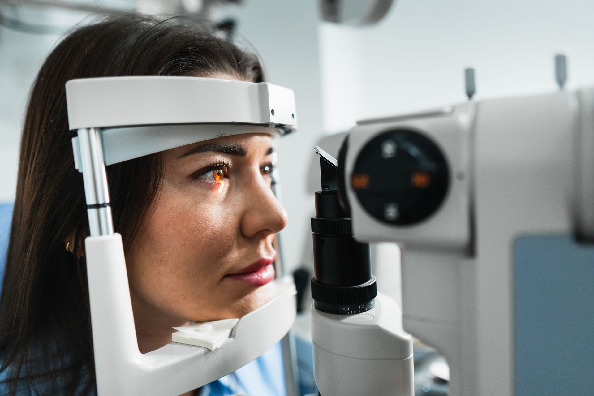 A young woman is going through an eye exam with an eye medical equipment scanning her eye. A young woman is going through an eye exam with an eye medical equipment scanning her eye.