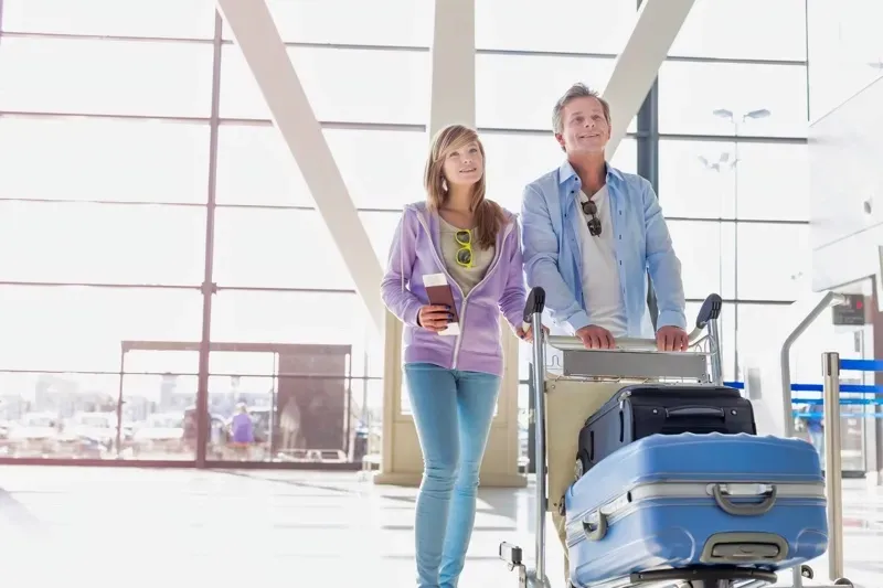 A man and a woman are walking through an airport with luggage.