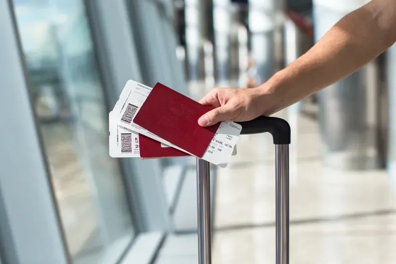 A person is holding a suitcase with tickets and a passport.