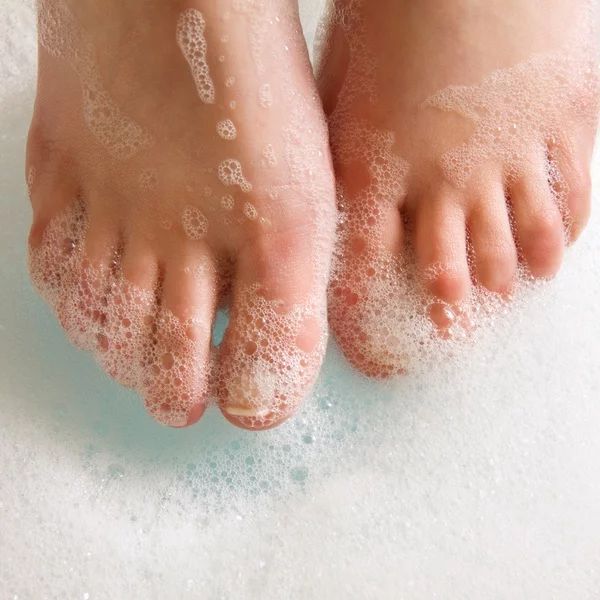 A person 's feet are covered in soap bubbles in a bathtub.