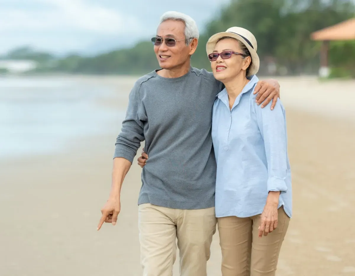 An elderly couple is walking on the beach.