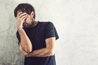 A man in a black shirt is covering his face with his hand.