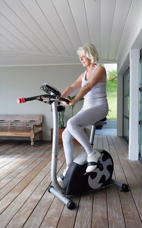A woman is riding an exercise bike on a wooden deck.