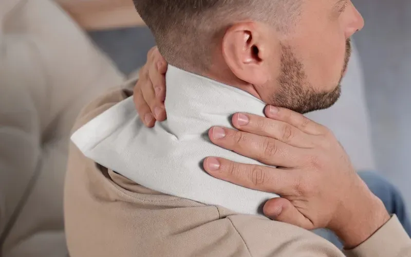 A man is laying on a couch holding an ice pack on his neck.