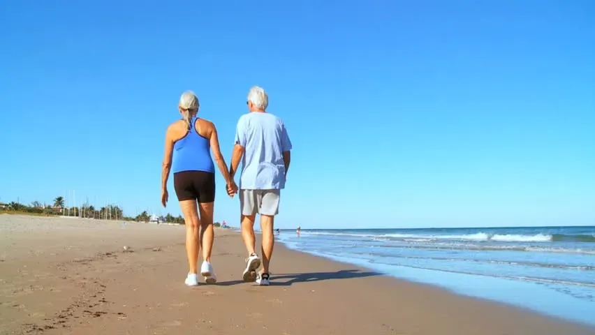 A man and a woman are walking on the beach holding hands.